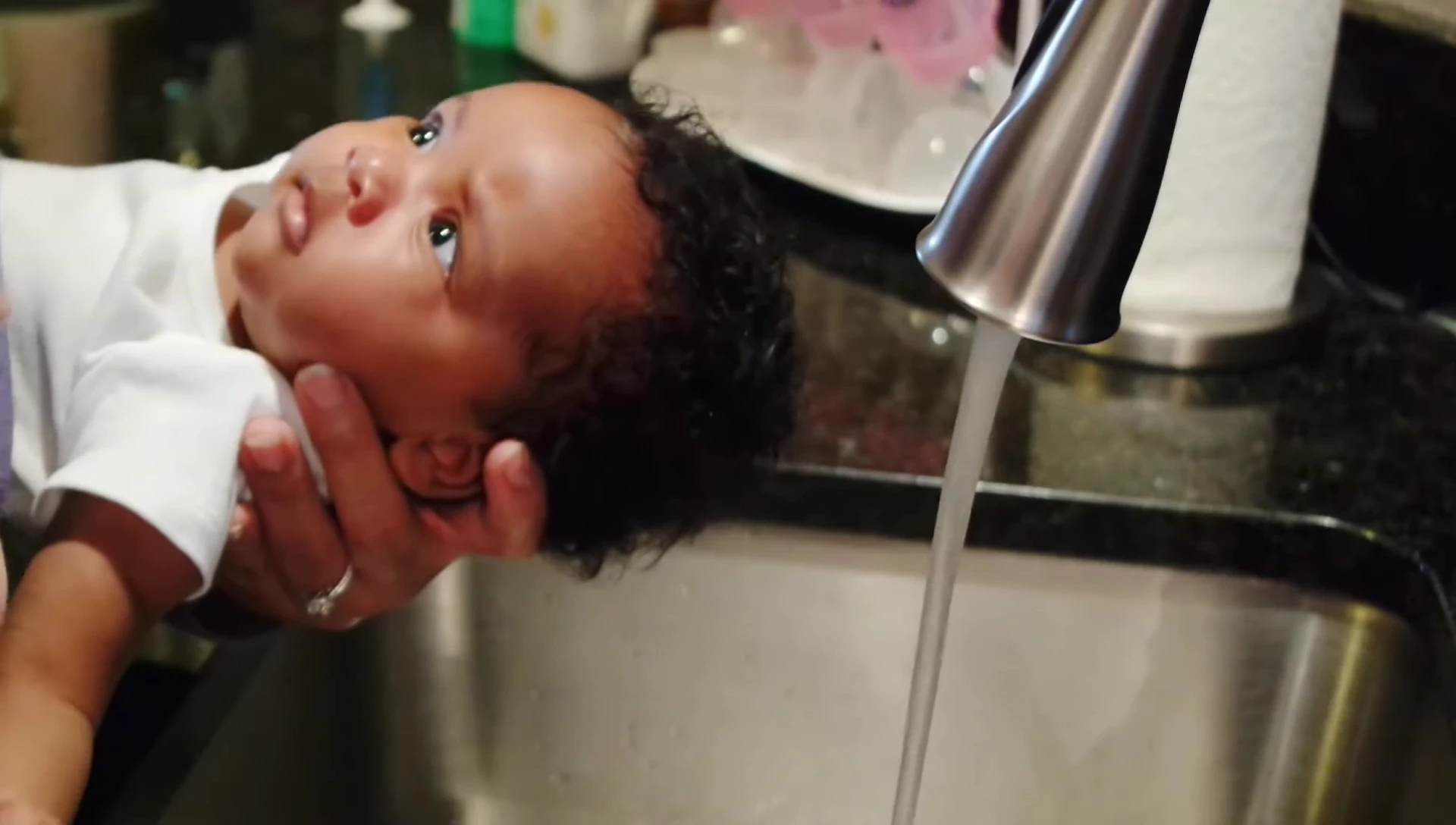 Rinsing baby's hair with warm water in the kitchen sink.