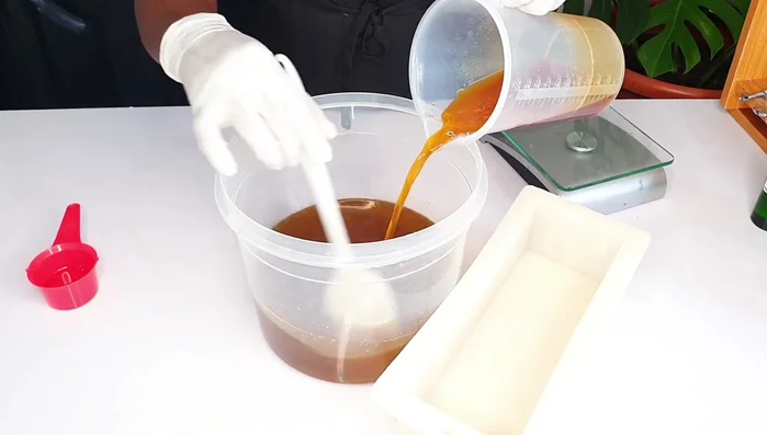 Slowly add the caustic soda solution to the melted oils, stirring continuously.