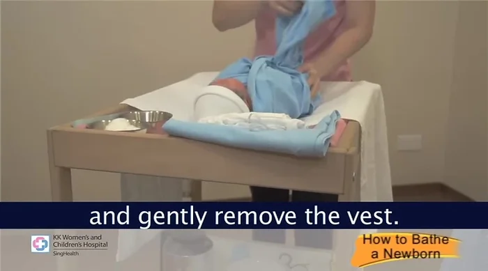 Prepare your baby: Place your baby on a bath towel and gently remove their vest. Talk to your baby to reassure them. Leave their diaper on and wrap them in the towel, keeping hands and feet covered.