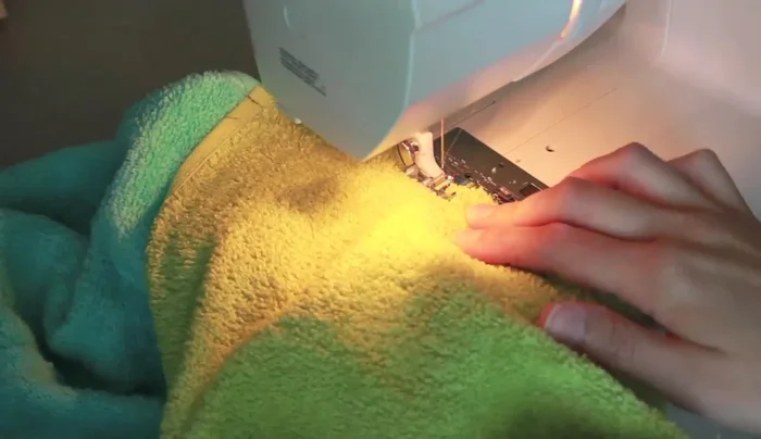 Zigzag stitch the seam between the hood and the bath towel to prevent fraying, using a dense zigzag stitch and backstitching.